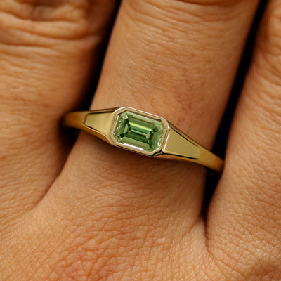 Close up view of a model's fingers wearing a 14k yellow gold emerald cut green lab created diamond Signet Ring