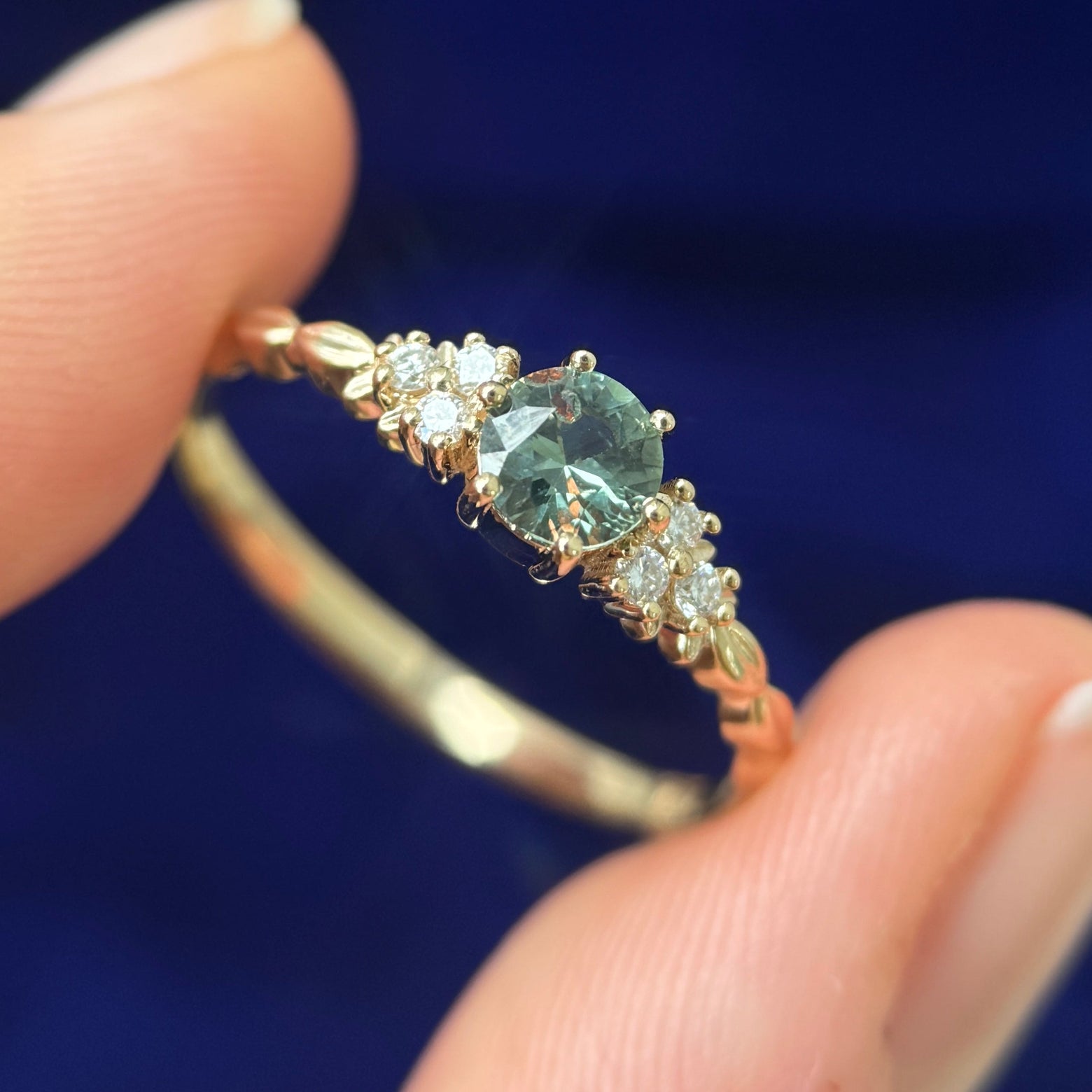 A model holding a 14k Yellow Gold Prongs-set 5mm Green Sapphire with 6pc white lab diamonds on Custom Leaves Band
