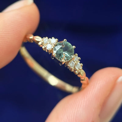 A model holding a 14k Yellow Gold Prongs-set 5mm Green Sapphire with 6pc white lab diamonds on Custom Leaves Band