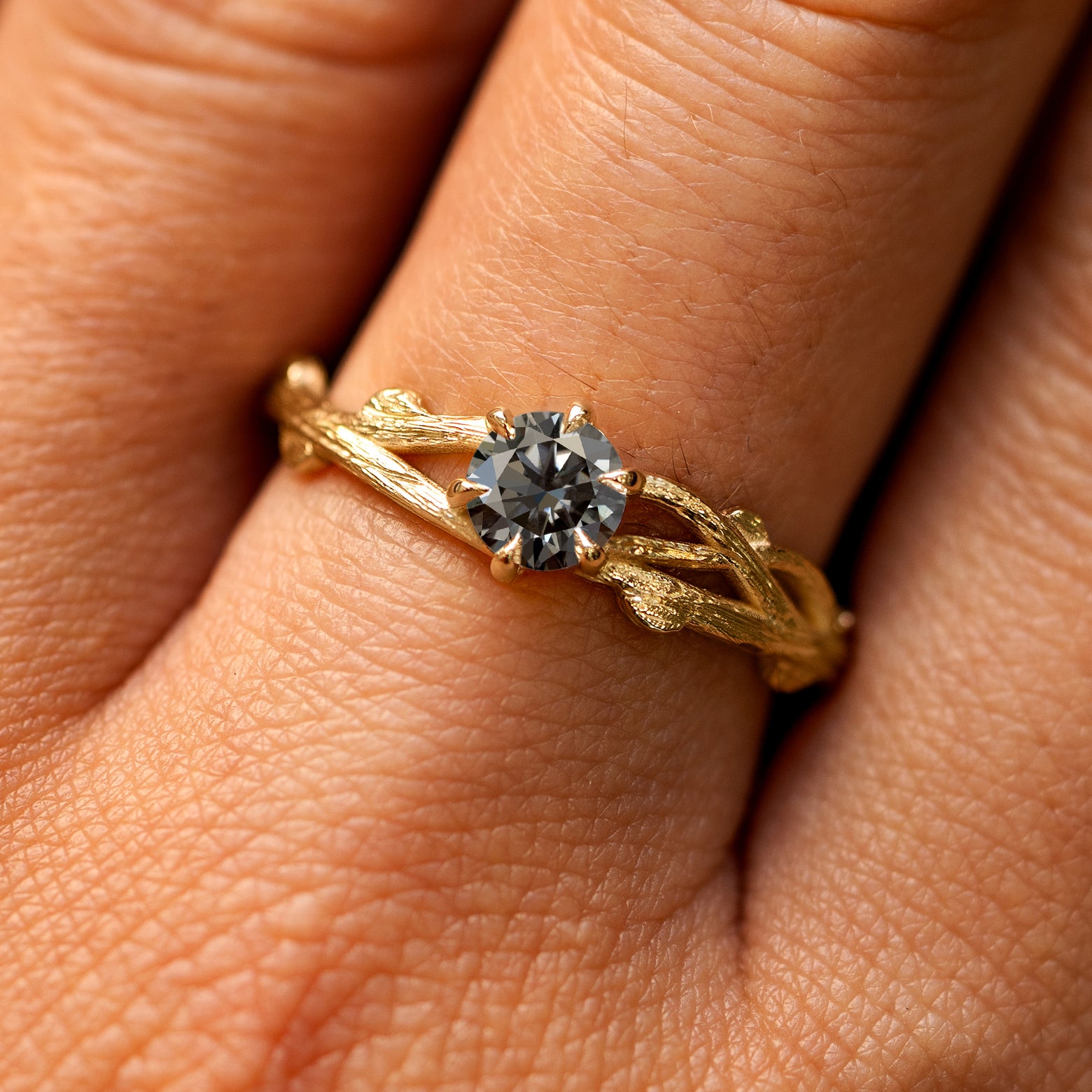Close up view of a model's fingers wearing a 14k yellow gold Grey Moissanite Branches Ring