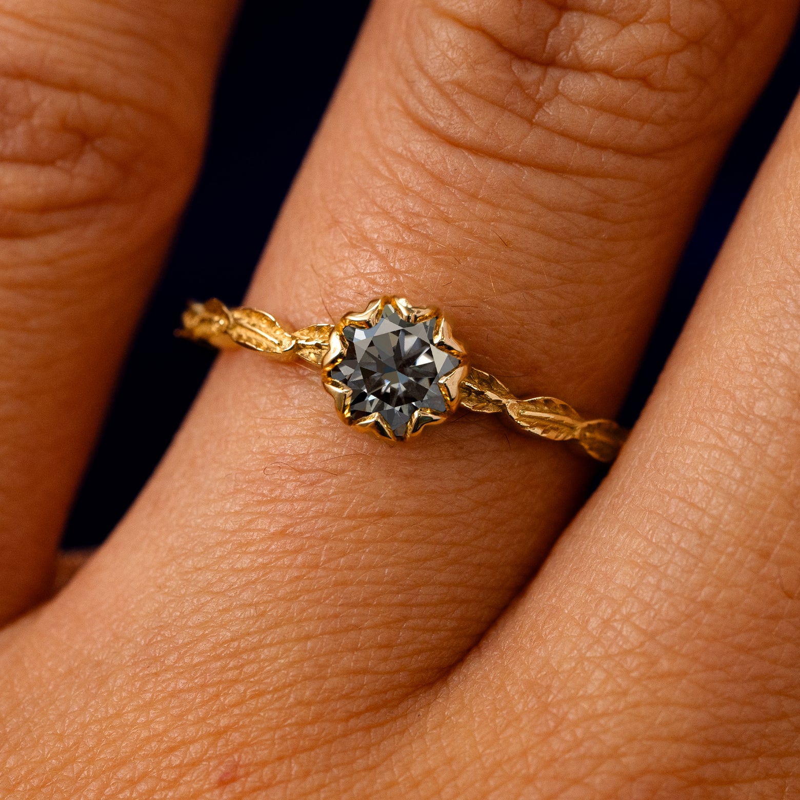 A solid 14k yellow gold Grey Moissanite Leaf Ring on a model's finger