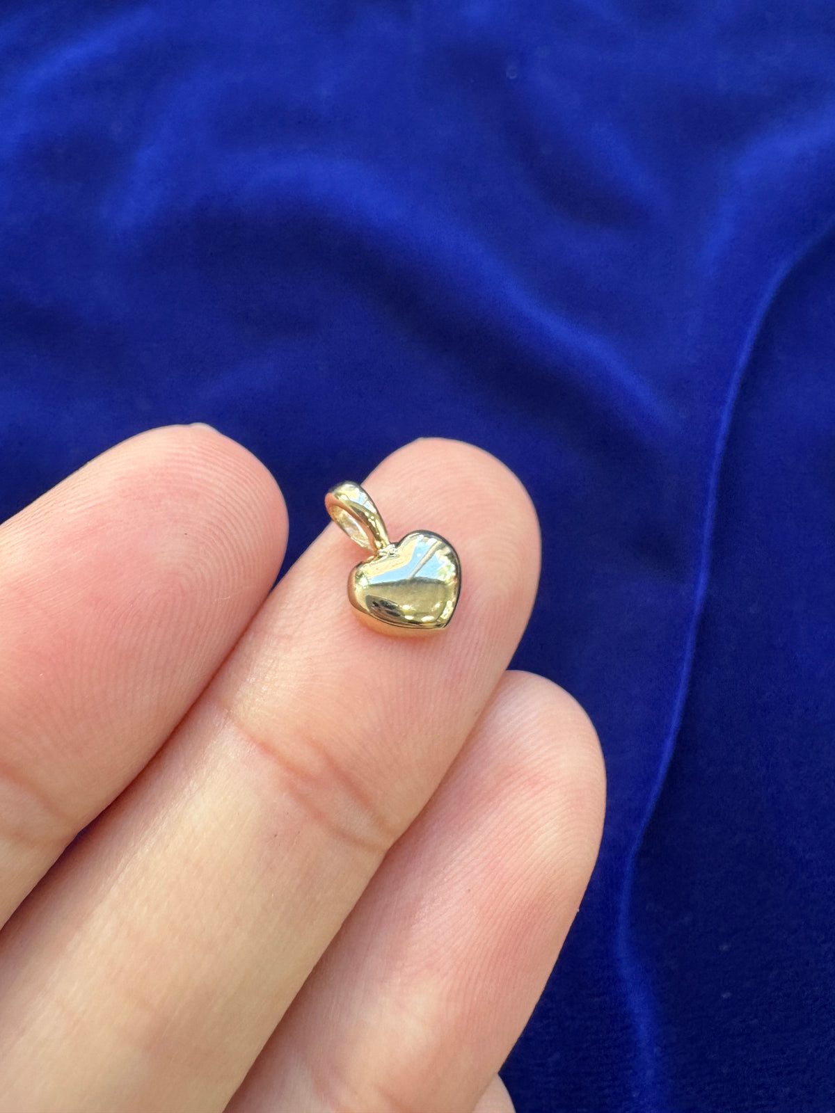 A solid 14k yellow gold heart charm pendant lying face up on a models finger