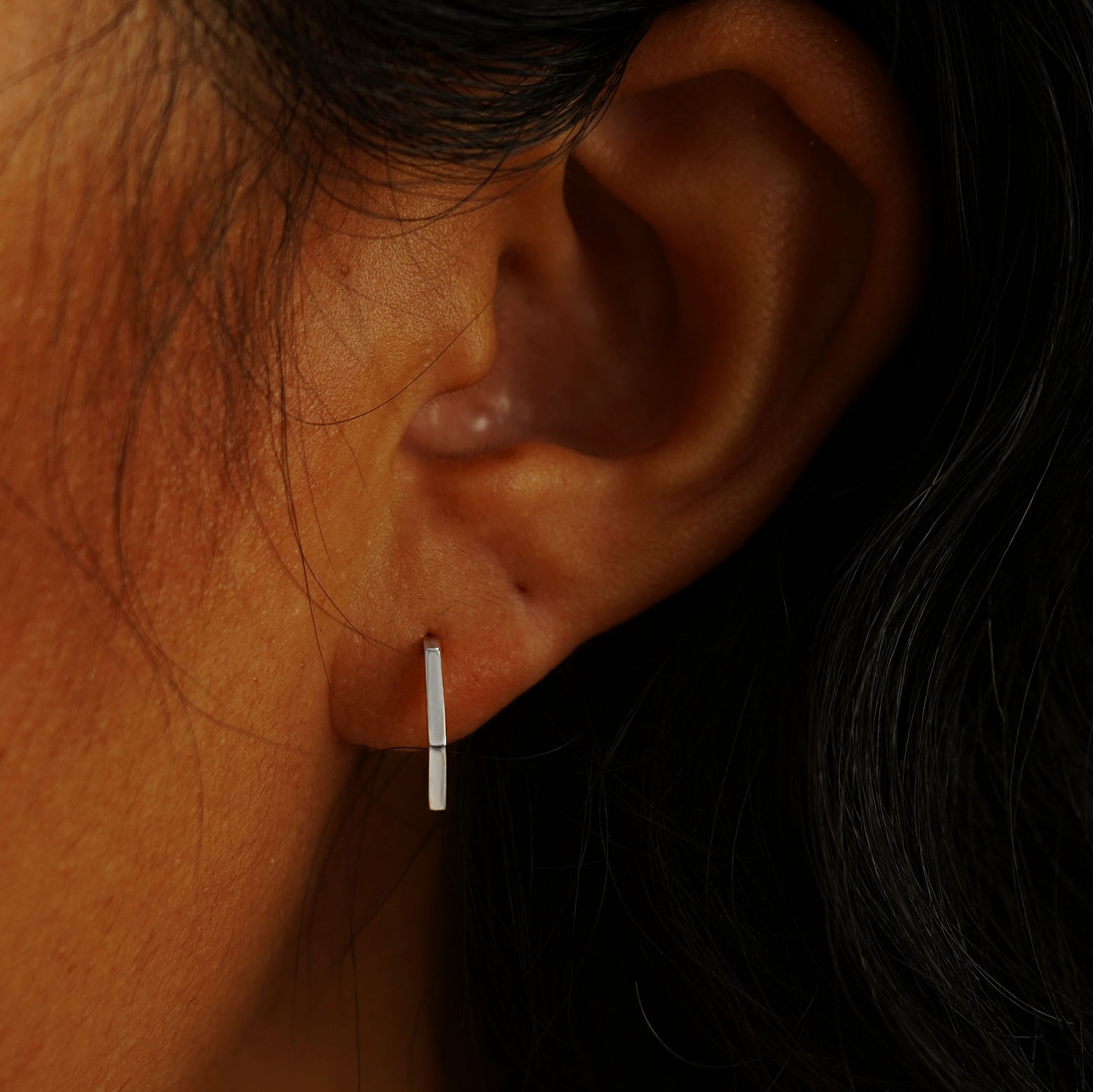 A model's ear wearing a 14 karat white gold Hexagon Huggie Hoop