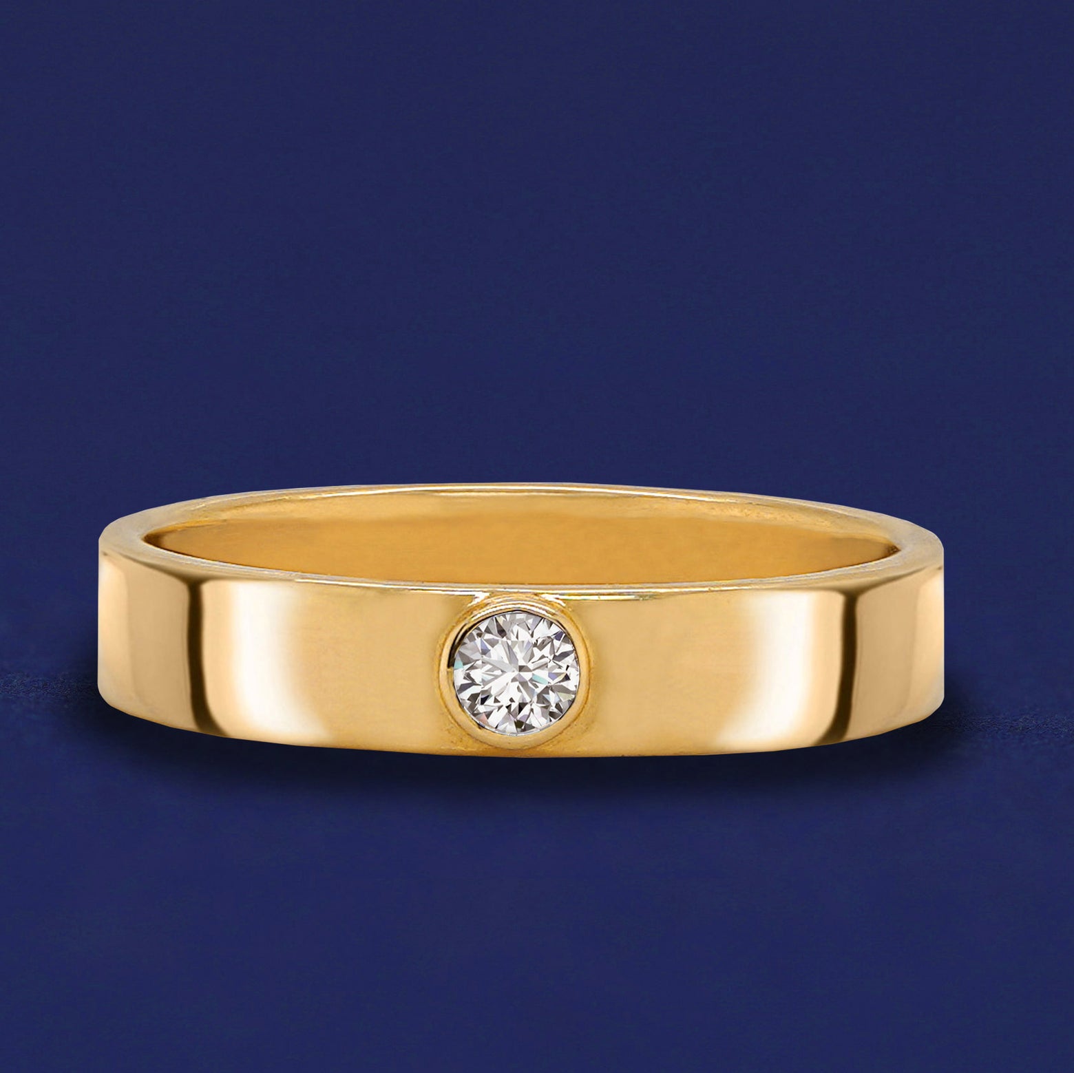 A 14 karat solid gold band ring with a bezel set Diamond on a dark blue background