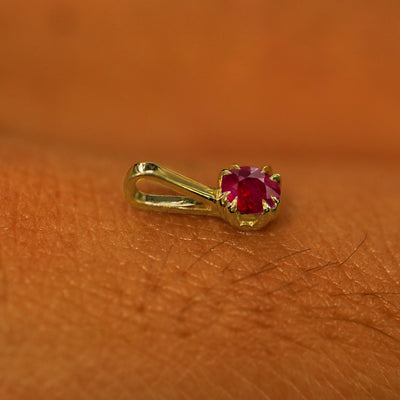 A 14k yellow gold Ruby Charm for chain resting on the back of a model's hand