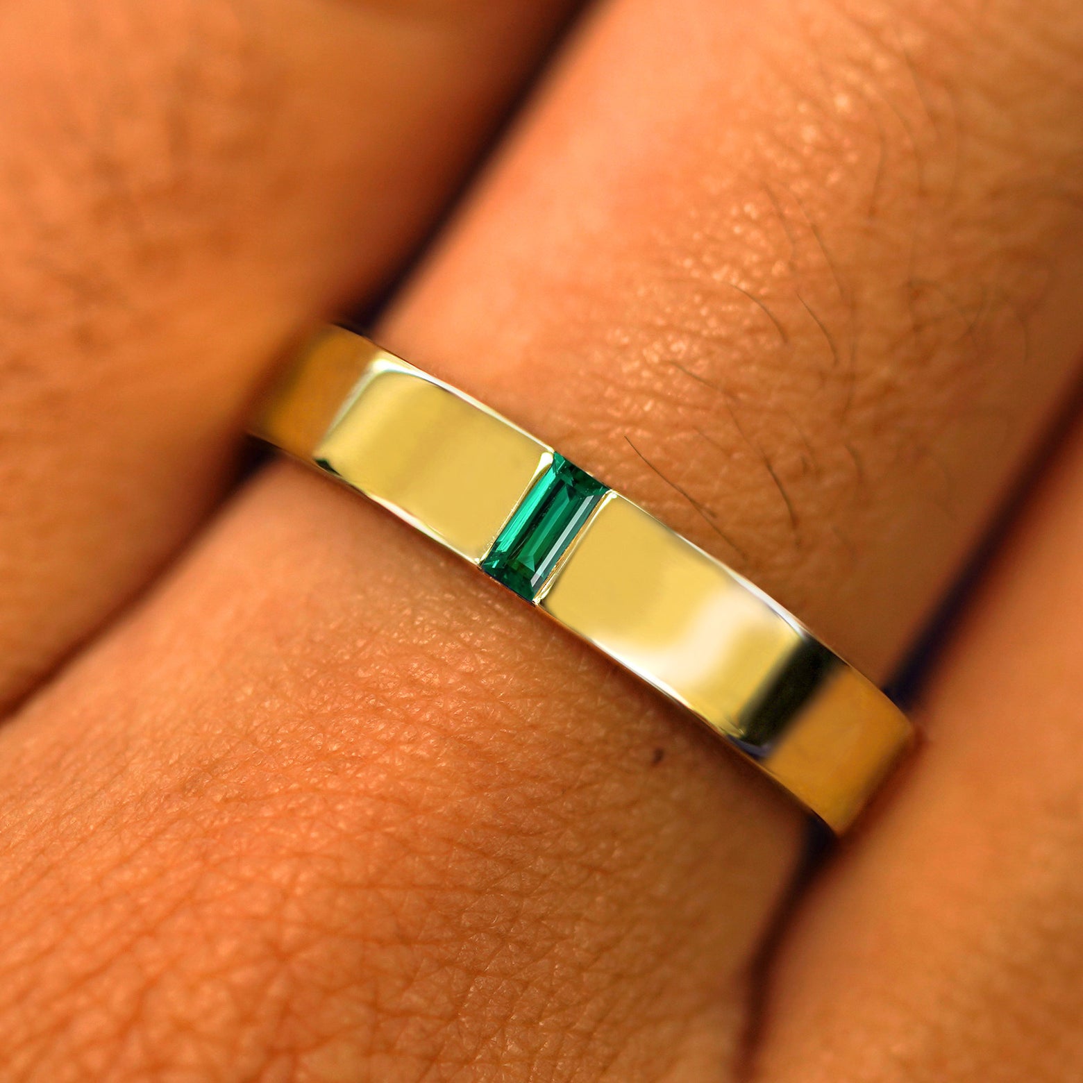 Close up view of a model's hand wearing a solid yellow gold Lab Emerald Baguette Band