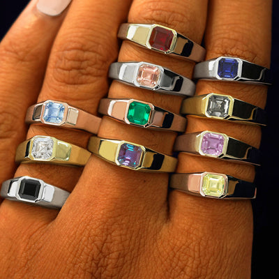 A hand wearing multiple lab gemstone signet rings in different metal and gem colors