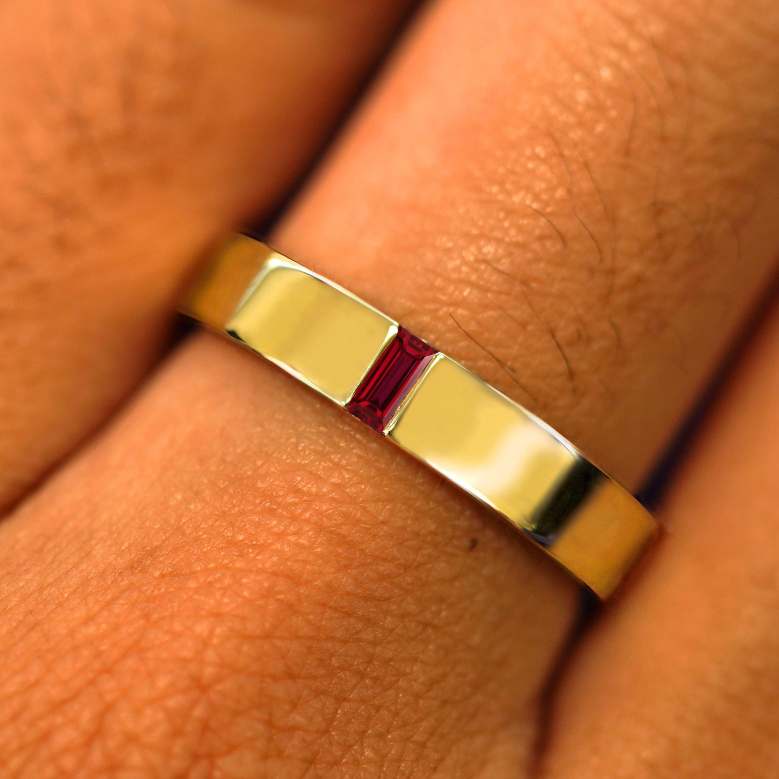 Close up view of a model's hand wearing a solid yellow gold Lab Ruby Baguette Band