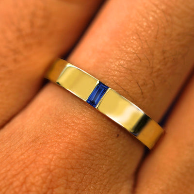 Close up view of a model's hand wearing a solid yellow gold Lab Sapphire Baguette Band