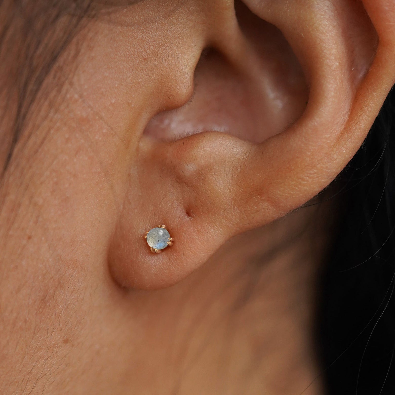 Close up view of a model's ear wearing a yellow gold labradorite earring