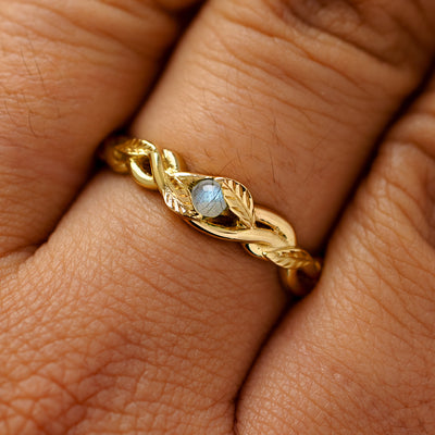A solid 14k yellow gold labradorite leaves and vines ring on a model's finger