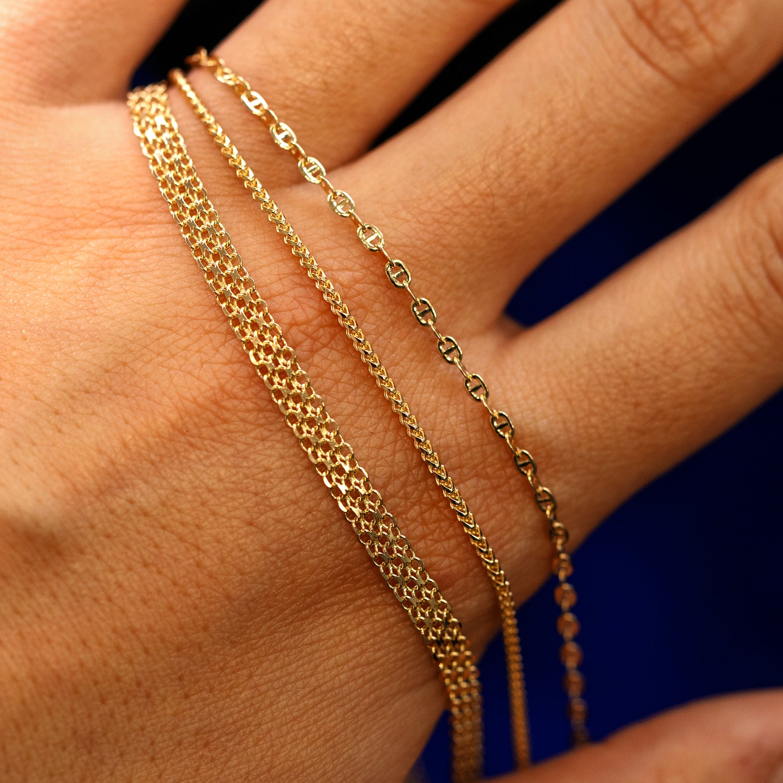 A models hand holding a Bismark Bracelet, a Mini Franco Bracelet, and a Flat Mariner Bracelet