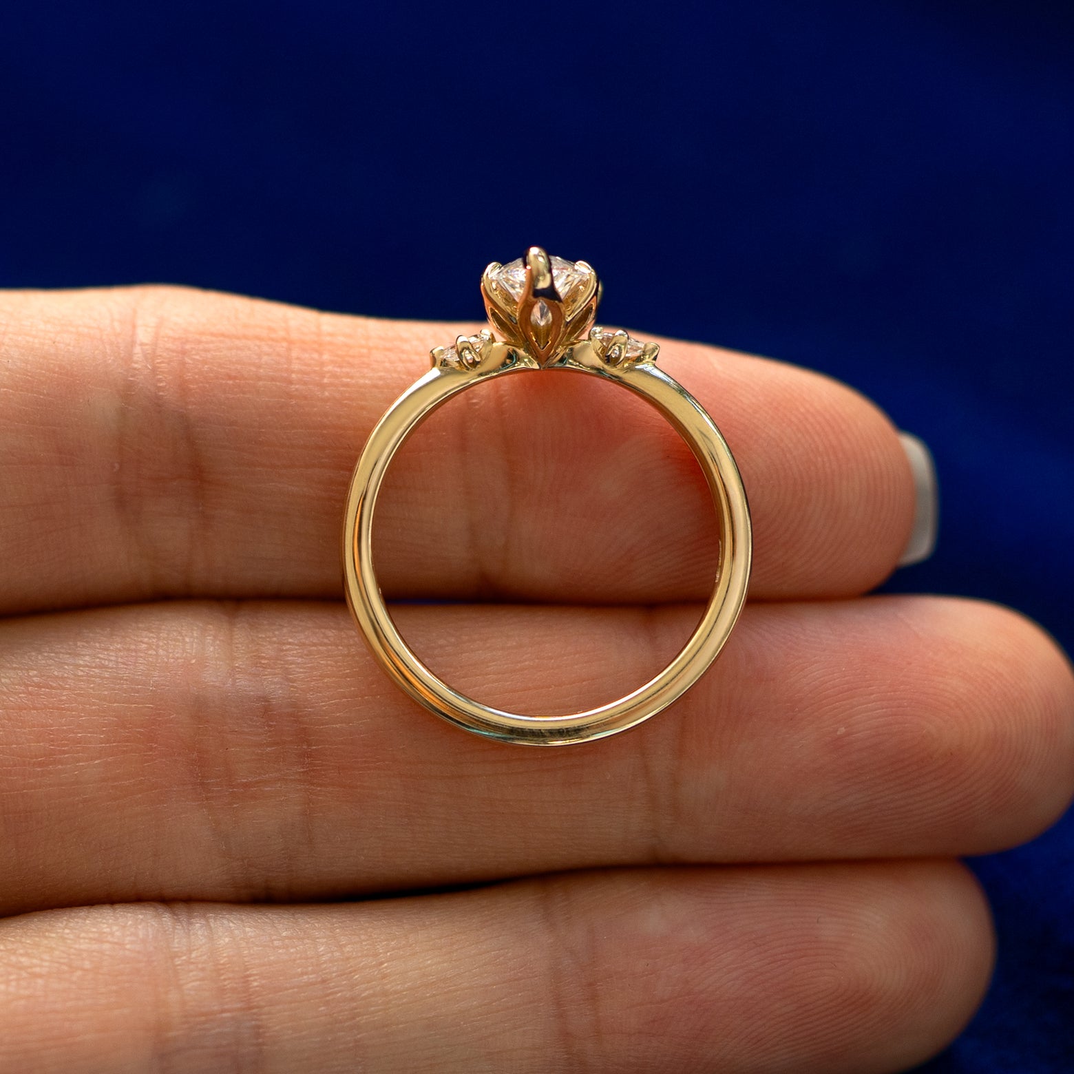 A yellow gold Marquise Lab Diamond Three Stone Ring in a model's hand showing the thickness of the band