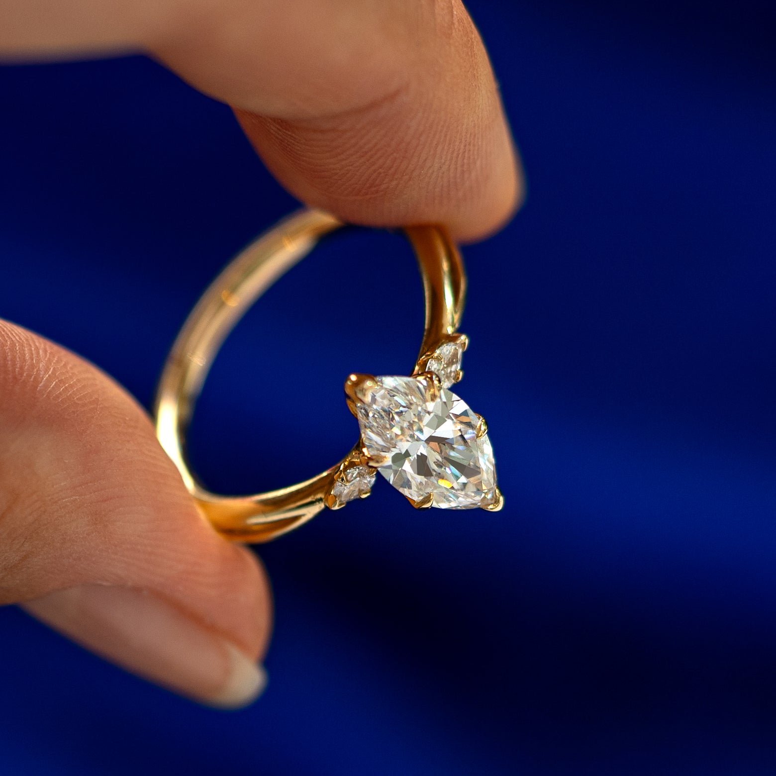 An angled view of a Marquise Lab Diamond Three Stone Ring on a model's finger to show the accent stones