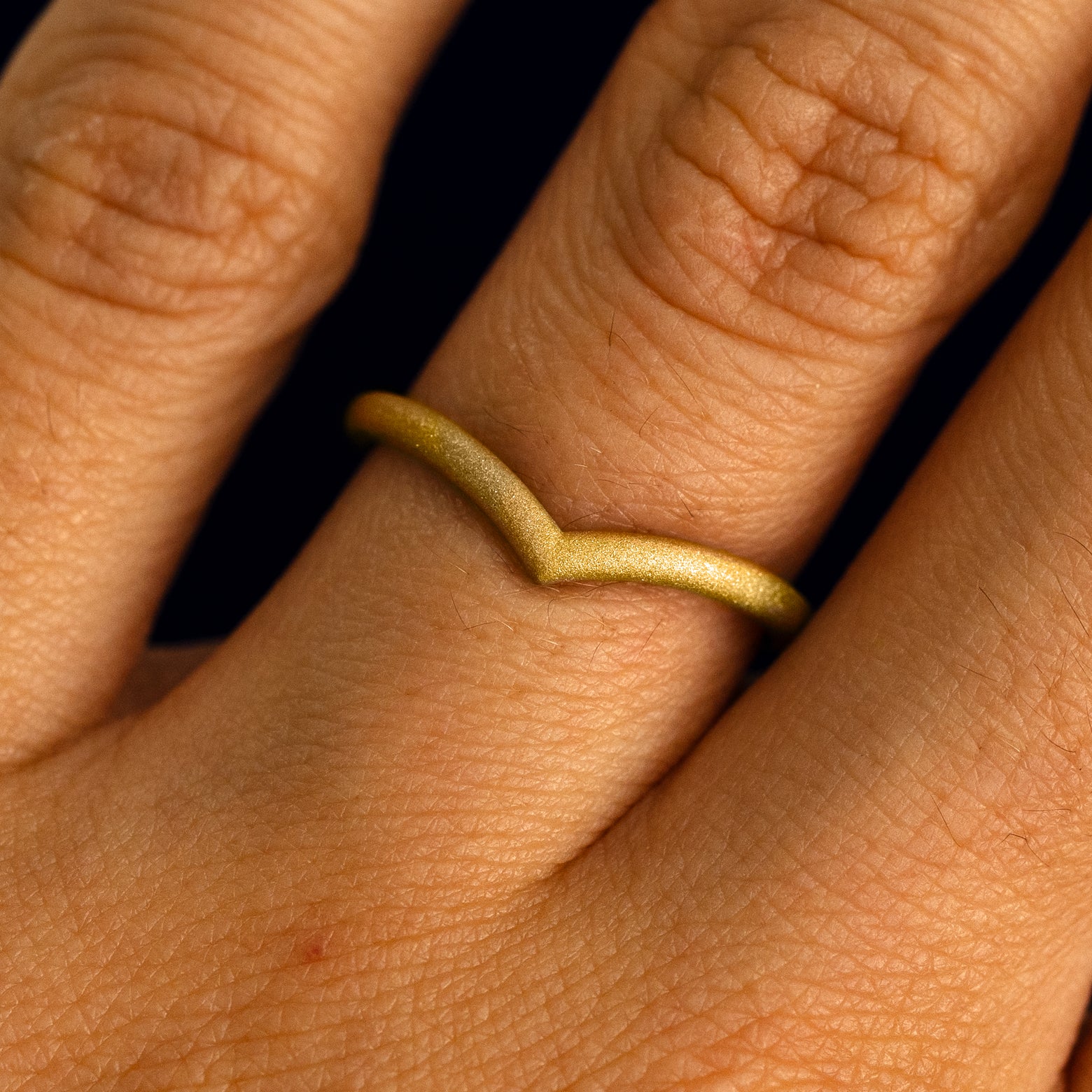 Close up view of a model's fingers wearing a 14k yellow gold matte finish Chevron Band