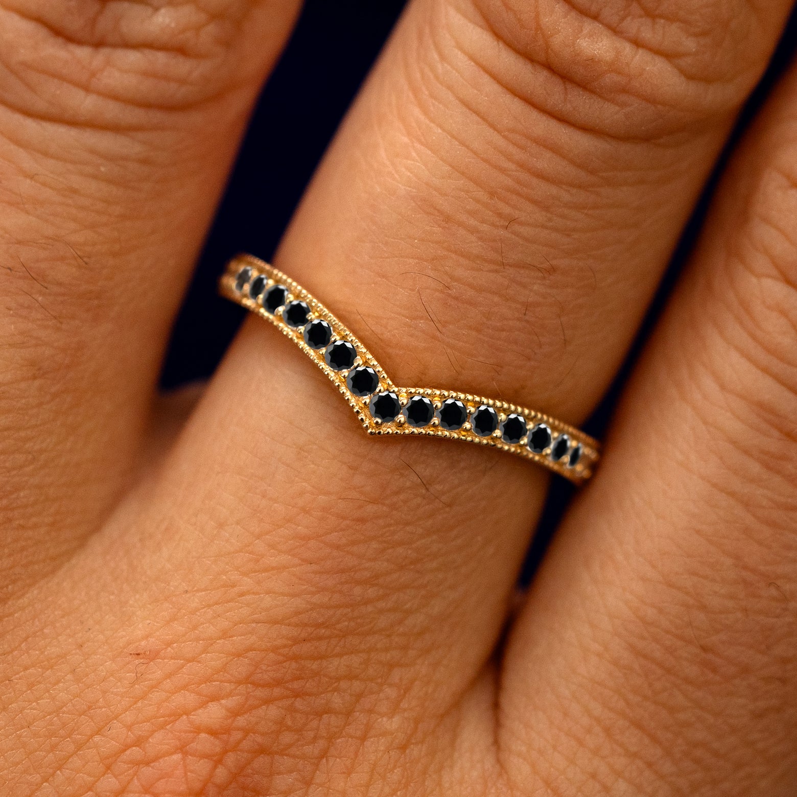 Close up view of a model's fingers wearing a 14k yellow gold Milgrain Pave Black Diamond Chevron Band