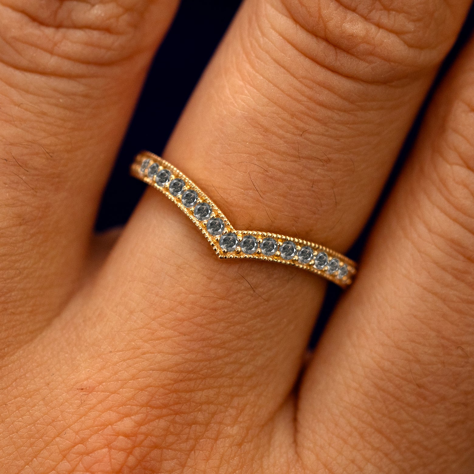 Close up view of a model's fingers wearing a 14k yellow gold Milgrain Pave Salt and Pepper Diamond Chevron Band