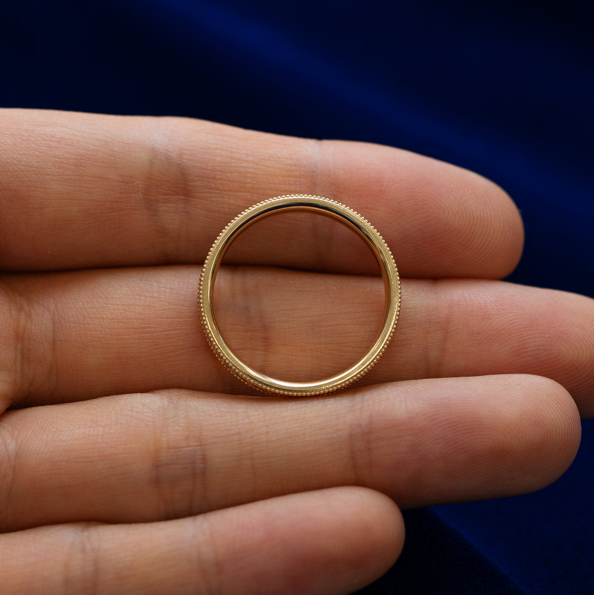 A milgrain scroll band lying flat in a models hand to show the thickness of the ring