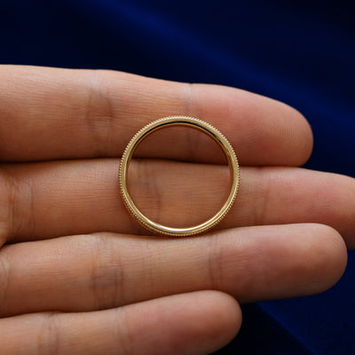 A milgrain scroll band lying flat in a models hand to show the thickness of the ring