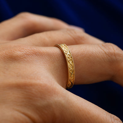 Side view of a model wearing a solid 14k yellow gold milgrain scroll band to show the raised engraving