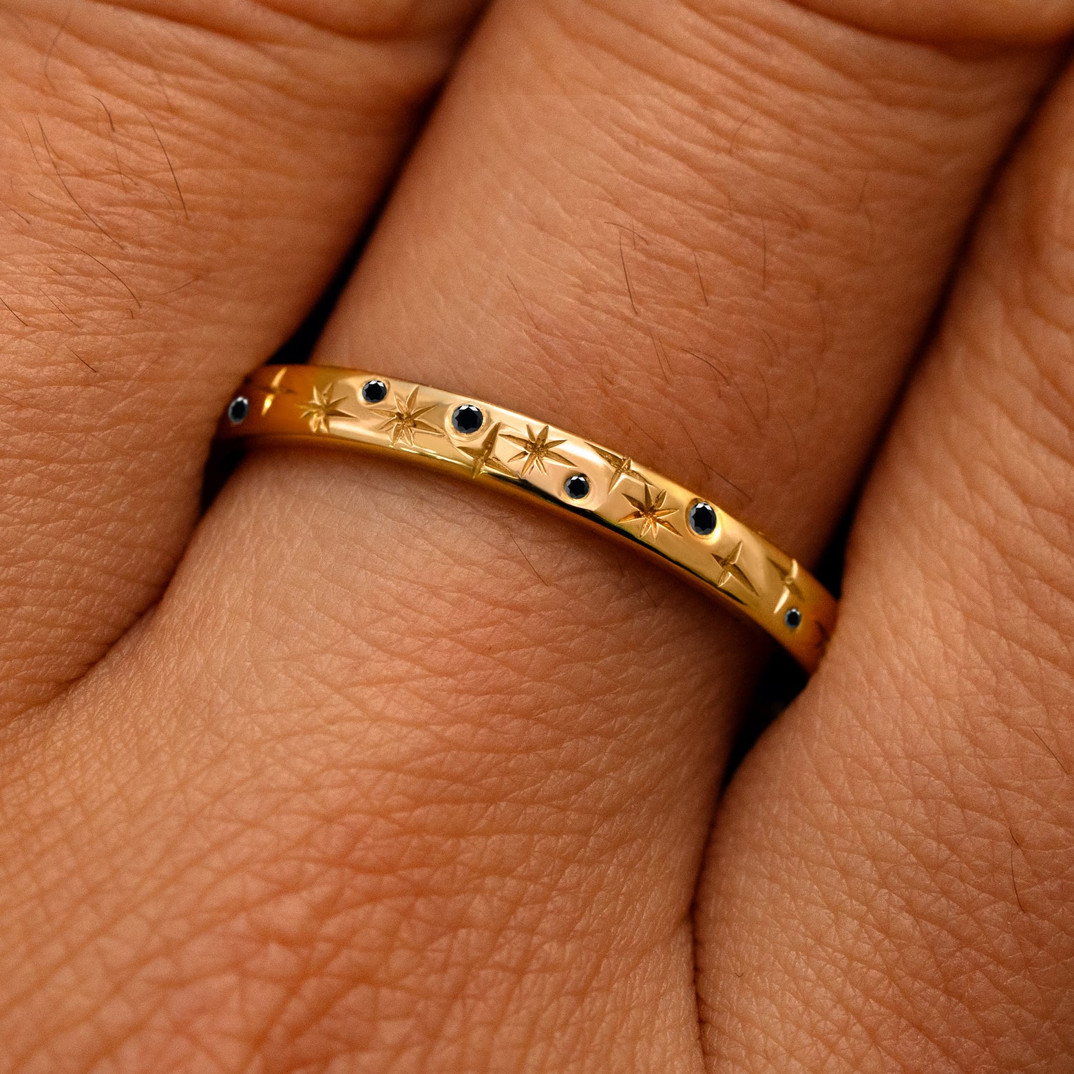 Close up view of a model's fingers wearing a 14k yellow gold Mixed Black Diamond Stars Band