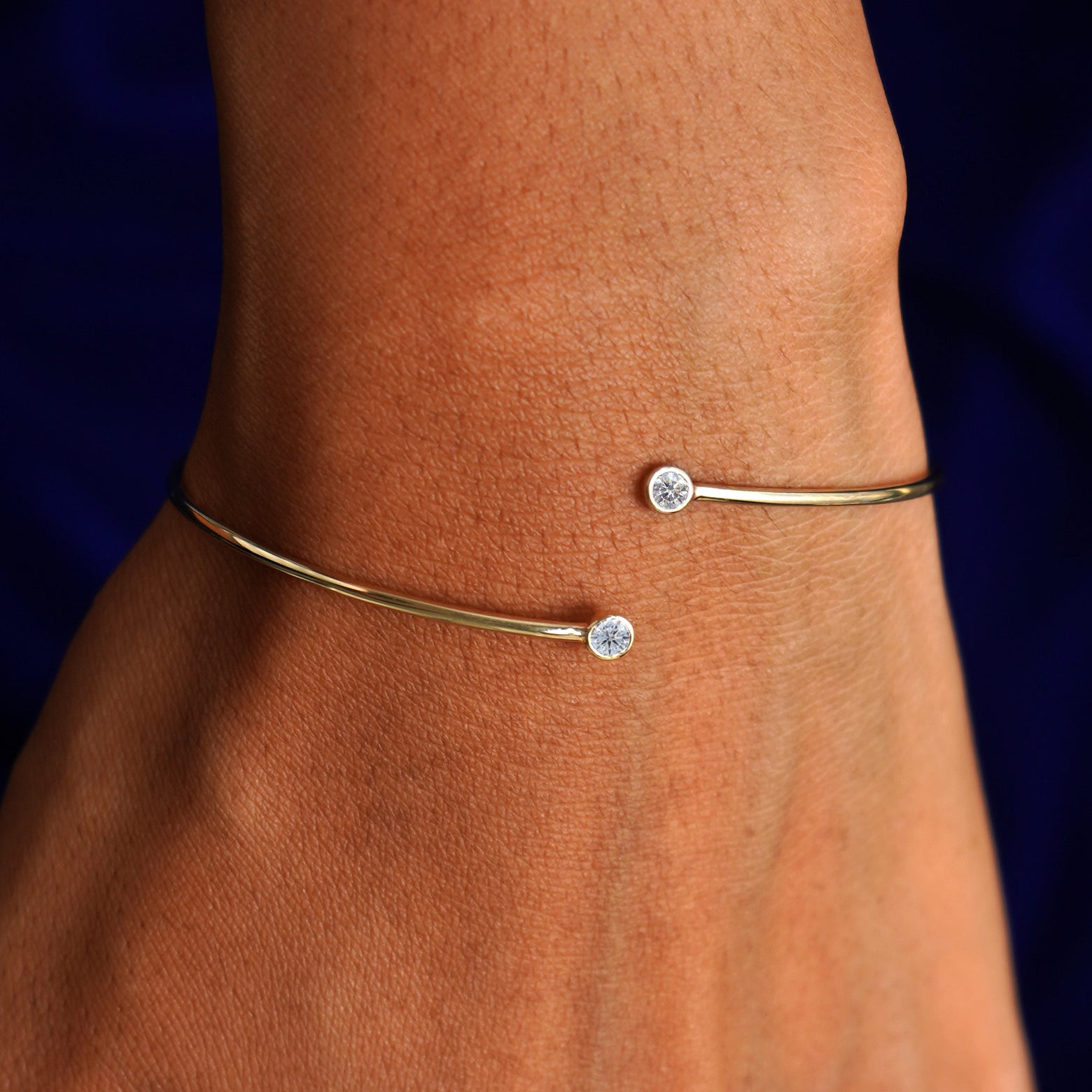 Close up view of a model's wrist wearing a 14k gold moissanite gemstone bypass bangle