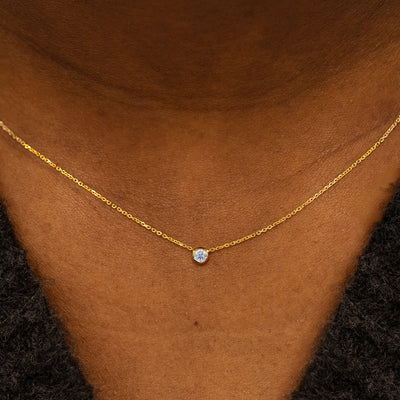 Close up view of a model neck wearing a 14k yellow gold Bezel set Moissanite gemstone necklace 