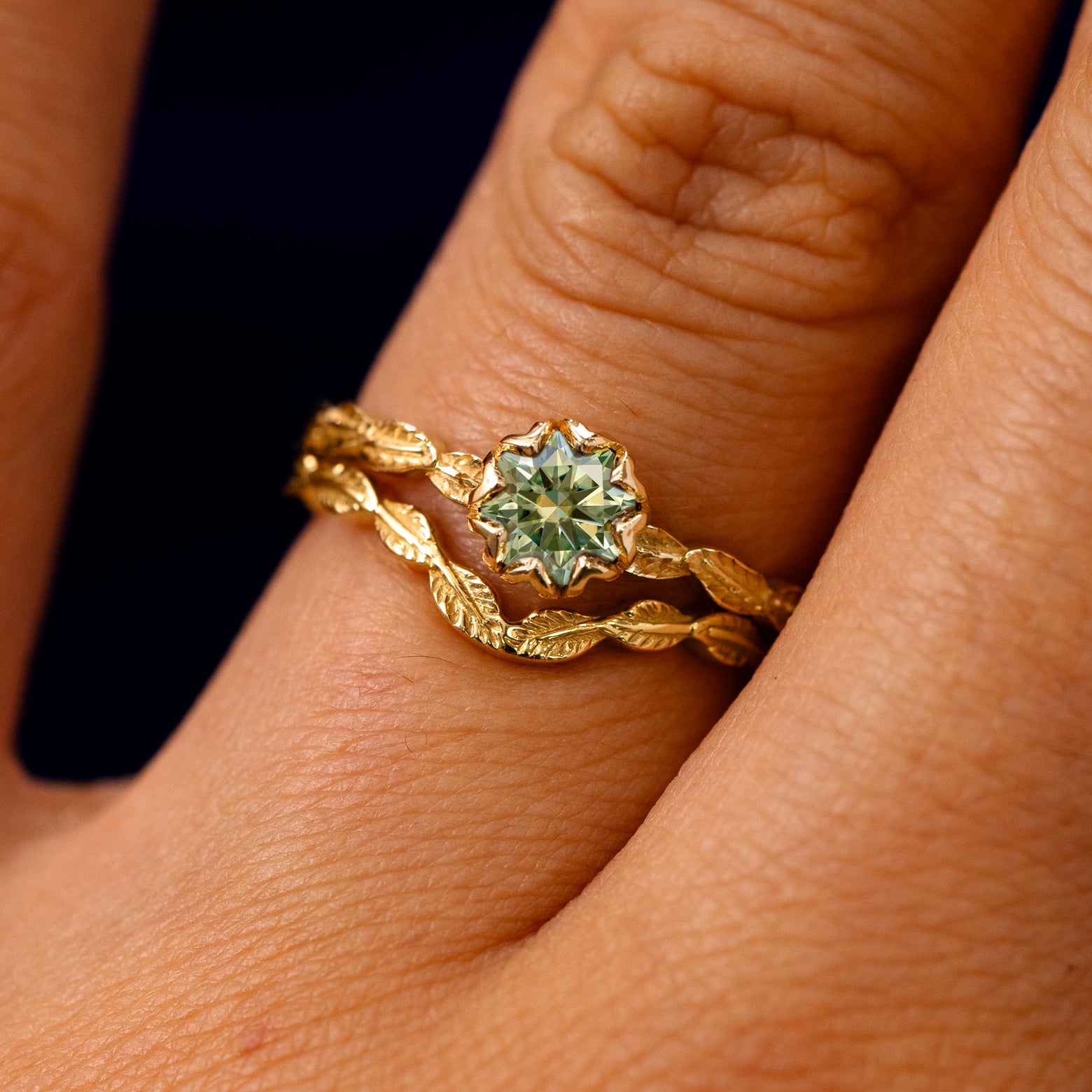 A model's fingers wearing a 14k yellow gold Green Moissanite Leaf Ring with Band