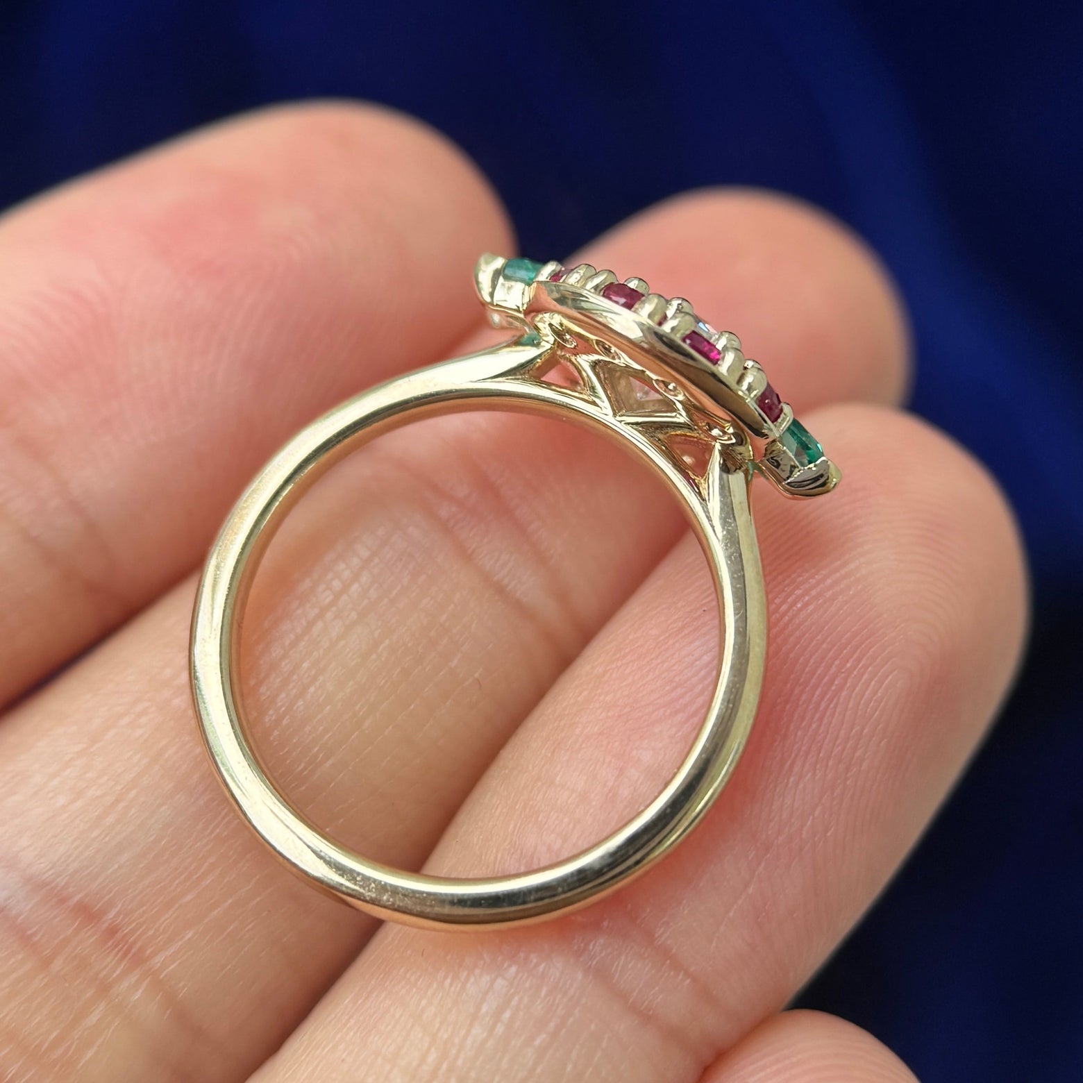 A 14k Yellow Gold and 5.5mm Round Moissanite with Marquise and Round Lab Rubies Custom Ring laying flat in a models hand to show the thickness of  the band