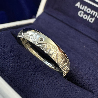 A photo of 950 Platinum Champagne Gold Flush-set 1.2mm Salt-and-pepper Diamond w/ Engraved Scotland, Tetons, Yosemite & Bennington Mountain Ranges All-around 4mm Curvy Mirror Band resting in a blue ring box