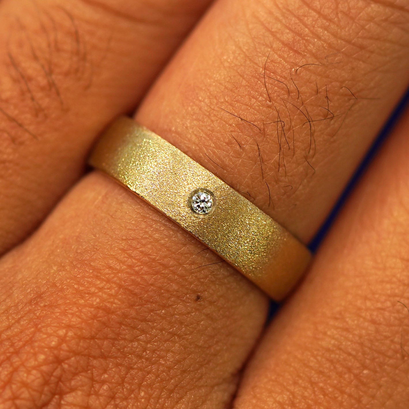 Close up view of a model's fingers wearing a 14k yellow gold Mix Stardust Band with one diamond