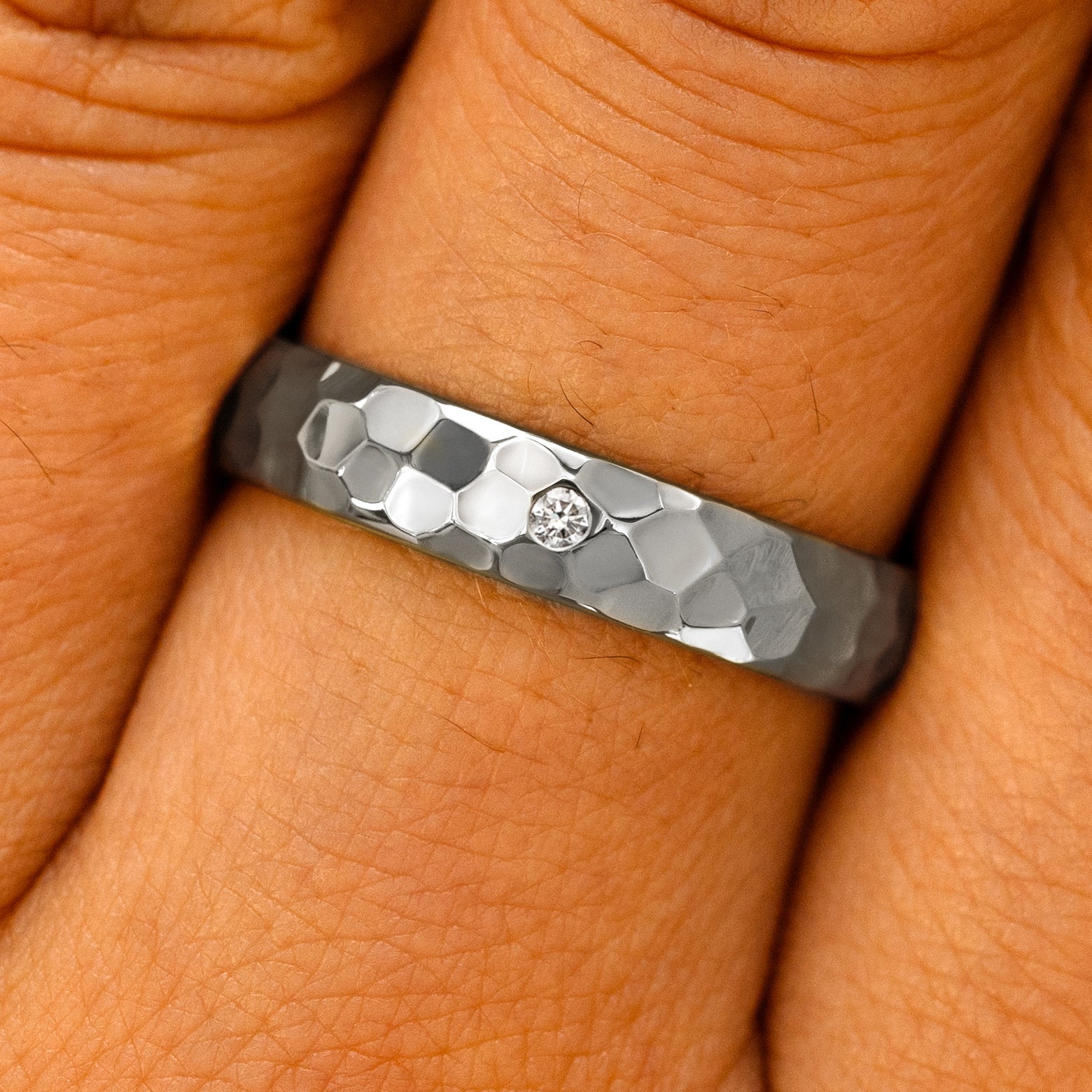 Close up view of a model's fingers wearing a Platinum Curvy Hammered Band with one diamond