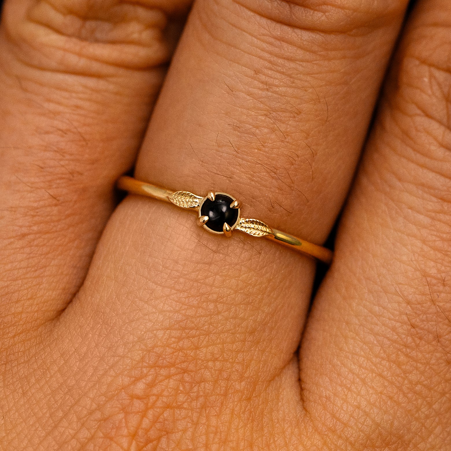 A solid 14k yellow gold Onyx Gemstone Two Leaf Ring on a model's finger