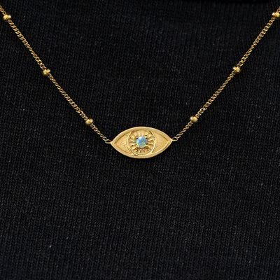 Close up view of a solid 14k yellow gold opal evil eye necklace against a model's black shirt