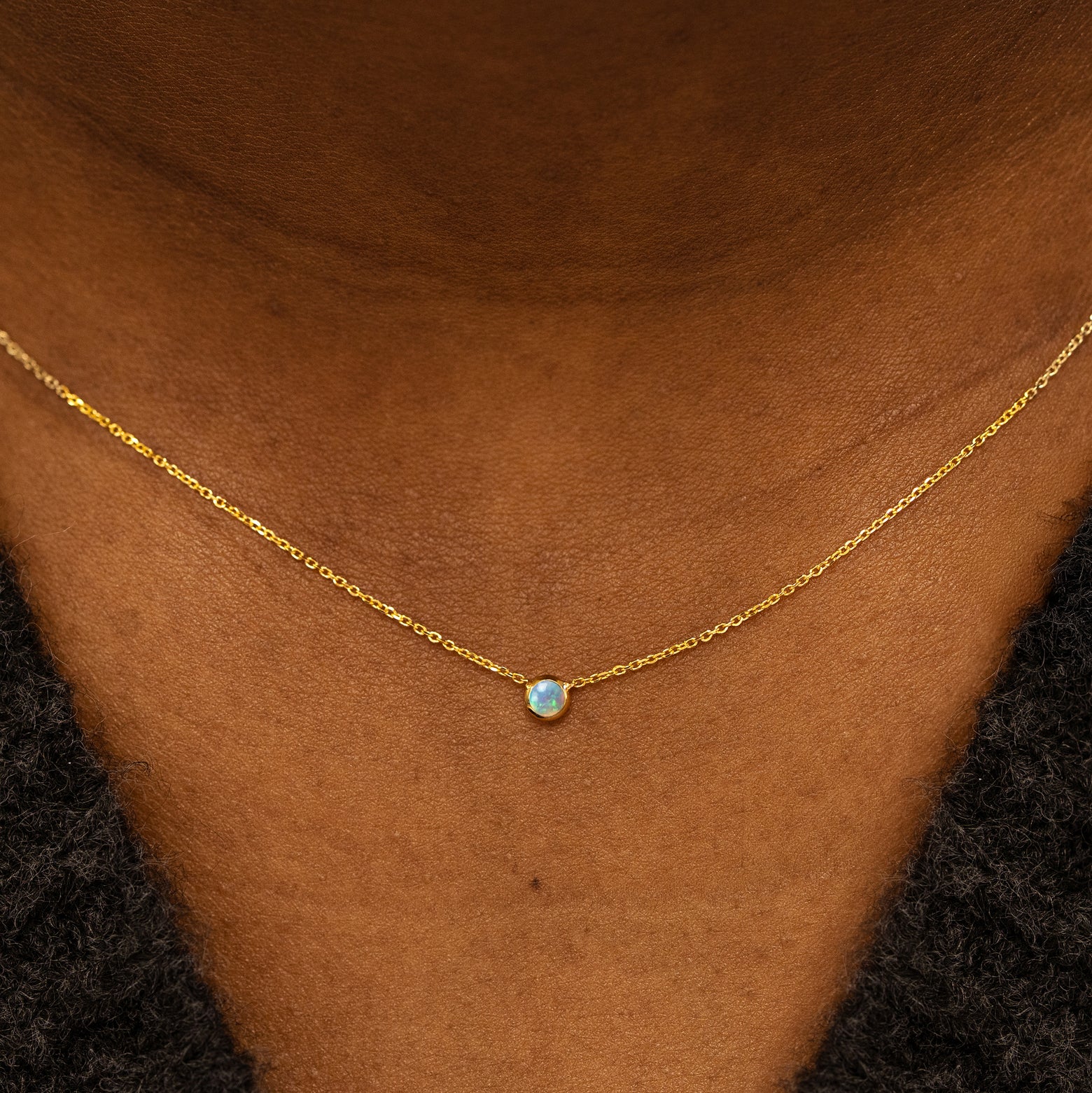Close up view of a model neck wearing a 14k yellow gold Bezel set Opal gemstone necklace 