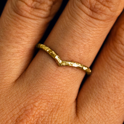 Close up view of a model's fingers wearing a 14k yellow gold organic finish Chevron Band