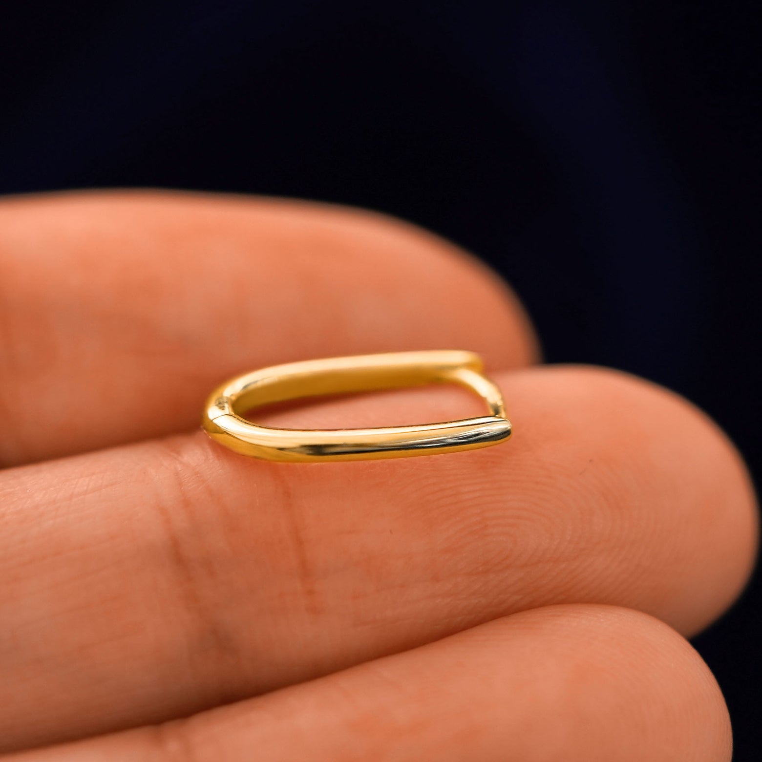 A 14 karat gold Oval Huggie Hoop laying on a model's fingertips on it's side