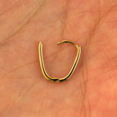 An open 14k yellow gold Oval Huggie Hoop resting in a model's palm