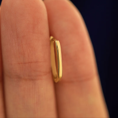 A 14k solid gold Oval Huggie Hoop between a model's fingers to show the thickness of the earring