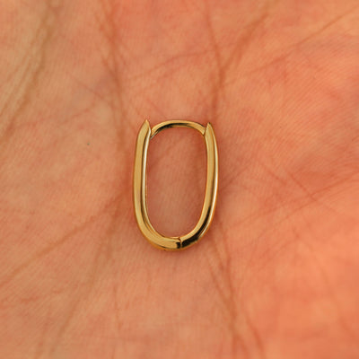 A single closed 14k yellow gold Oval Huggie Hoop resting in a model's palm