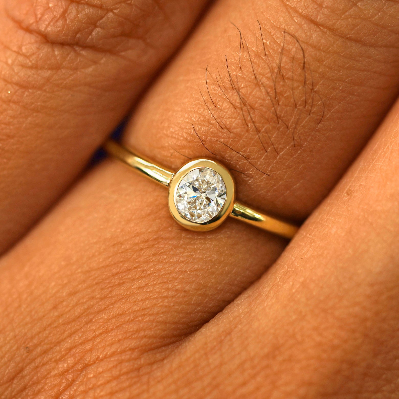 Close up view of a model's fingers wearing a 14k yellow gold Oval Lab Clear Diamond Ring