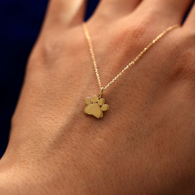 A solid 14k gold paw charm on a cable chain draped over the back of a models hand