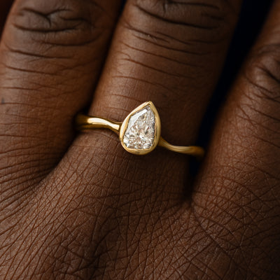 Close up view of a model's hand wearing a 14k yellow gold pear clear lab diamond liquid ring