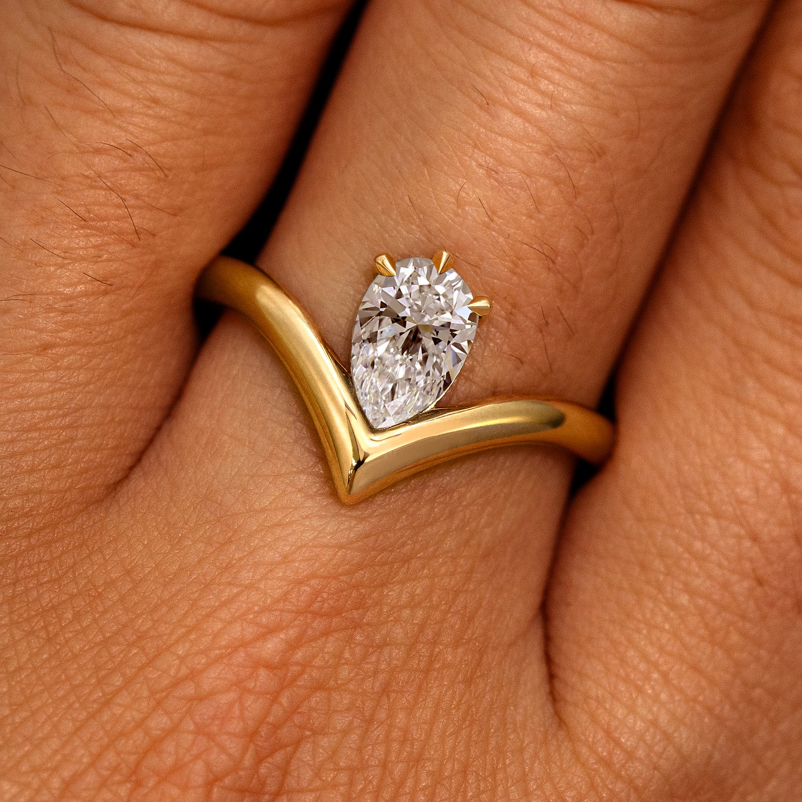 A model's hand wearing a 14k yellow gold Pear Clear Diamond Chevron Ring