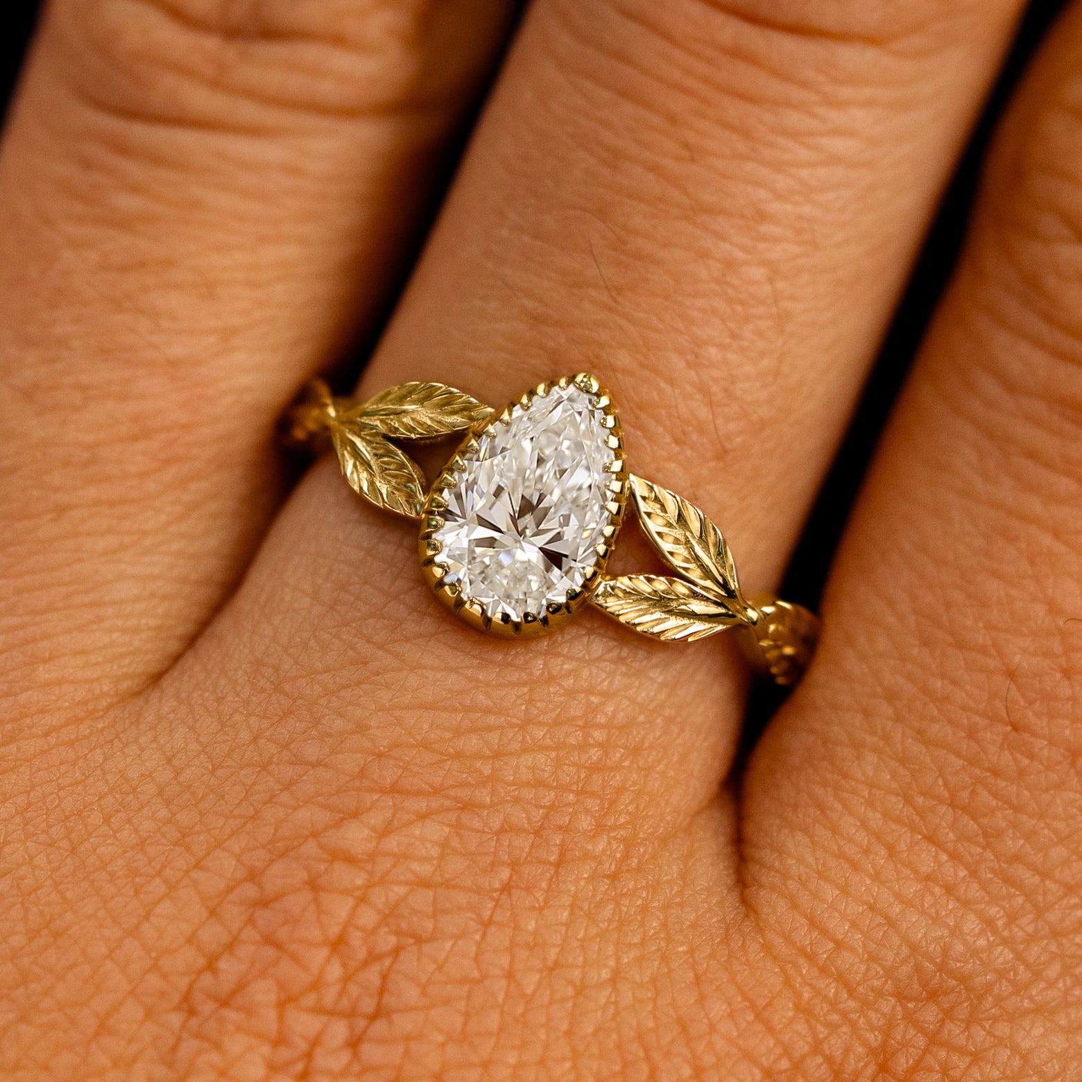 Close up view of a model's fingers wearing a 14k yellow gold Pear Lab Clear Diamond Leaves Ring