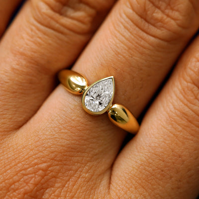 Close up view of a model's hand wearing a 14k yellow gold pear lab diamond engagement ring