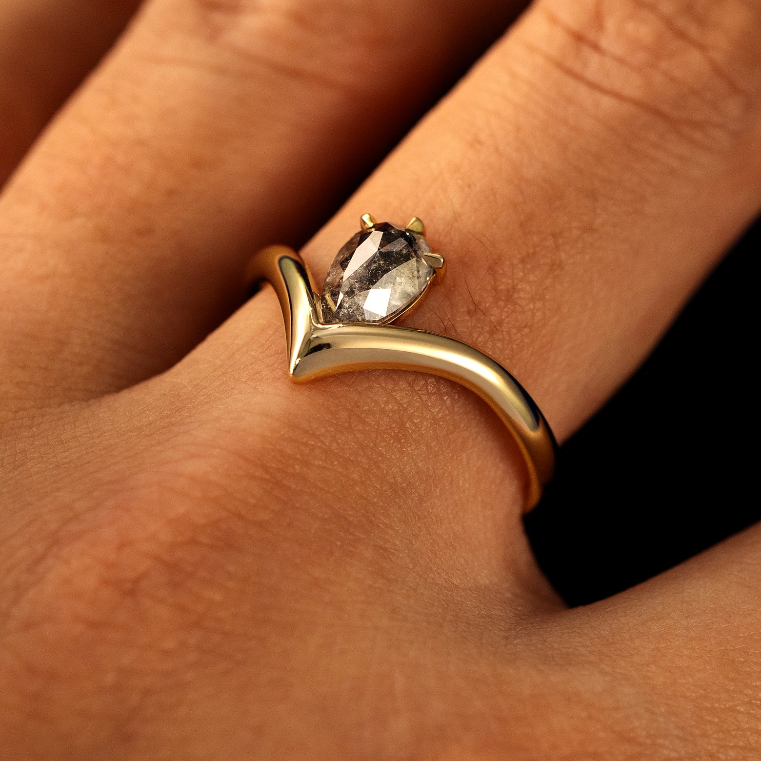 Side view of a solid 14 karat gold Pear Salt and Pepper Diamond Chevron Ring on a model's finger
