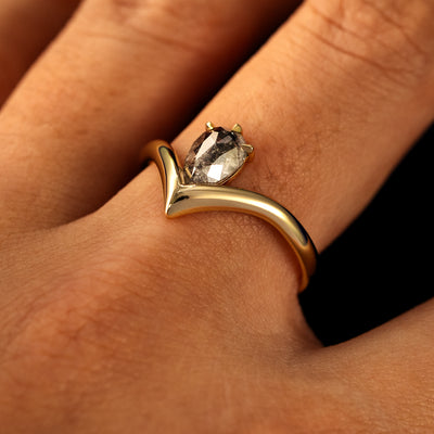 Side view of a solid 14 karat gold Pear Salt and Pepper Diamond Chevron Ring on a model's finger