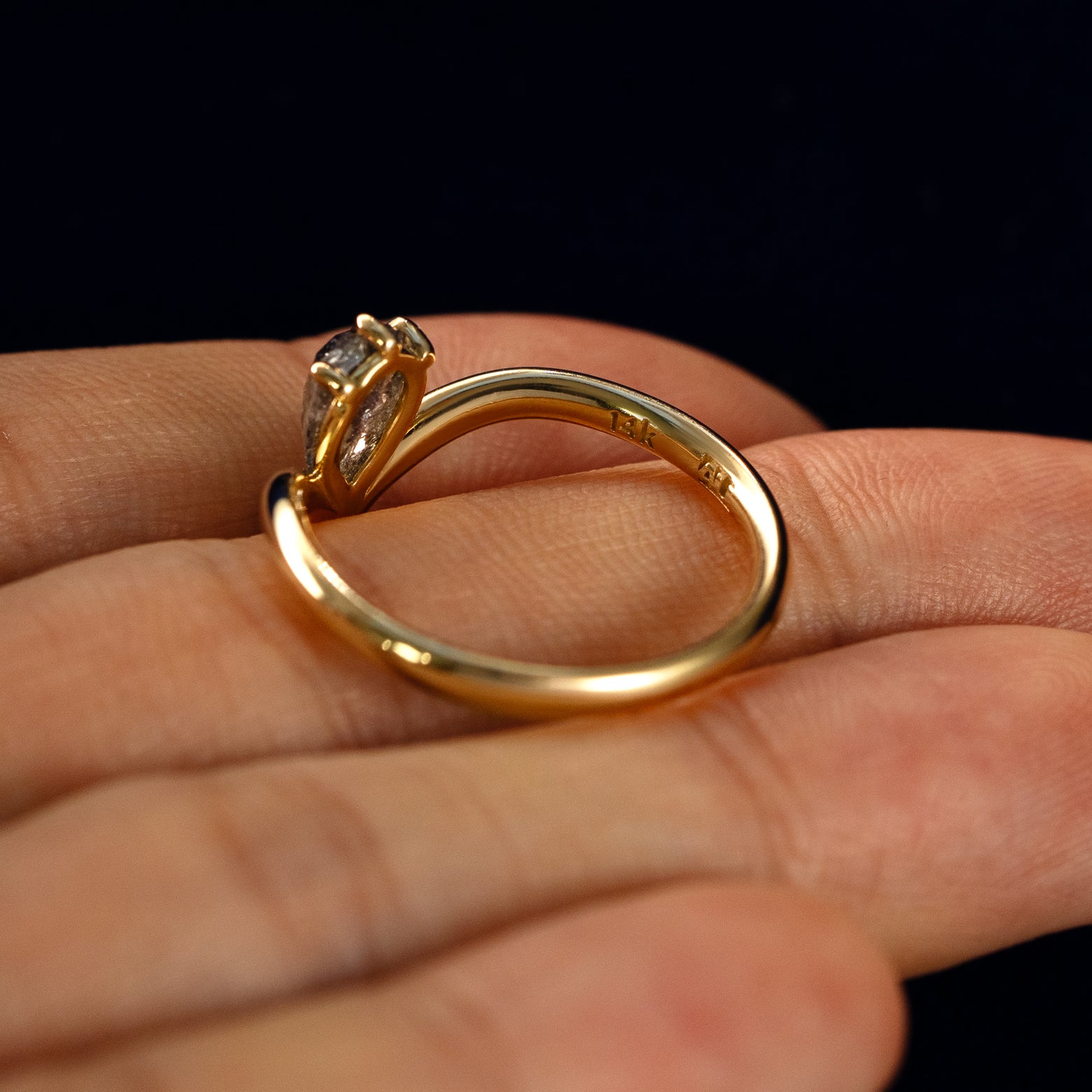 A Pear Salt and Pepper Diamond Chevron Ring in a model's hand showing the underside of the stones