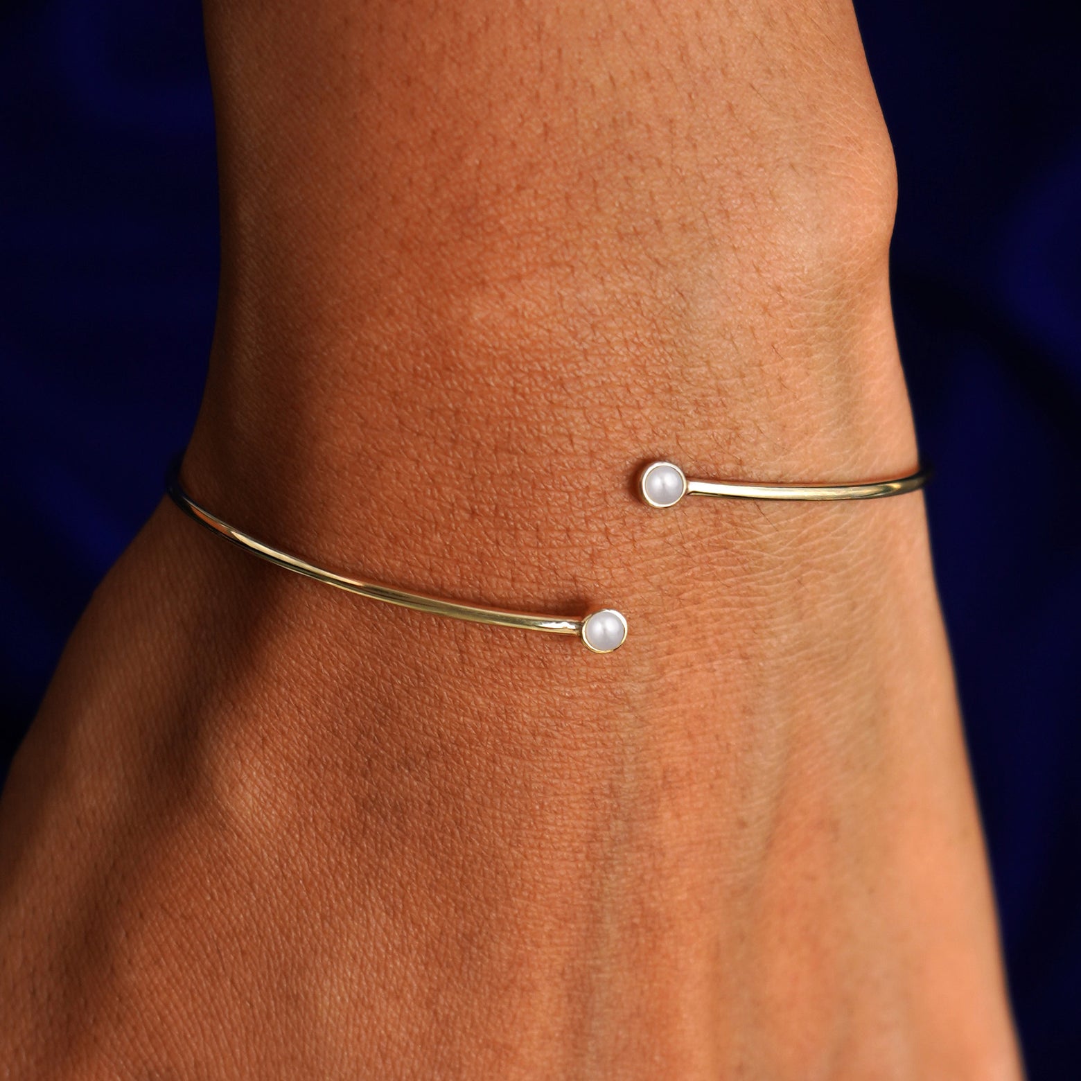 Close up view of a model's wrist wearing a 14k gold pearl gemstone bypass bangle